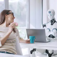 Kobieta z pączkiem i kubkiem kawy rozmawia z robotem przy laptopie. Oryginalna scena z przyszłości.
