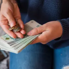 Dłonie liczą banknoty i monety, przygotowując się do wypłaty pensji.
