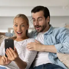 Para ogląda na telefonie, śmiejąc się z głupich pytań. Ich miny wyrażają zdziwienie i rozbawienie.