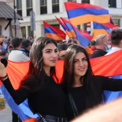 Dwie młode ormianki dumnie prezentują flagę narodową na tle tłumu.