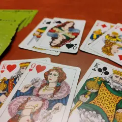 Karty do gry leżą na drewnianym stole. Król i królowa serc, król i królowa karo, król trefl. Może to gra w tysiąc zasady 2 osoby?
