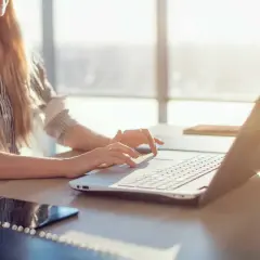 Kobieta z blond włosami pracuje na laptopie w słoneczny dzień.