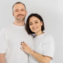 Uśmiechnięta para w białych koszulkach. Ona kładzie dłoń na jego piersi. Pewnie zastanawiają się nad śmiesznymi pytaniami.