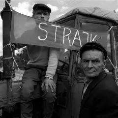 Dwóch mężczyzn w czapkach na tle traktora z banerem "STRAJK".