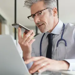 Lekarz w okularach rozmawia przez telefon, pracując przy laptopie.