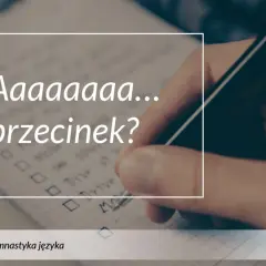 Długa litera "a" i pytanie "przecinek?" na tle notatnika, gdzie ręka pisze długopisem.