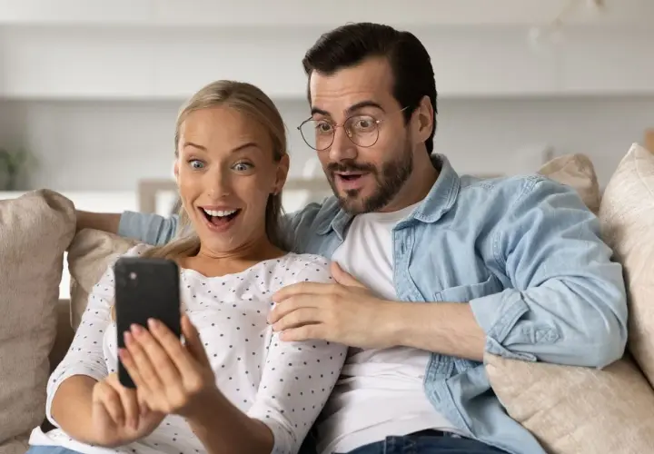Para ogląda na telefonie, śmiejąc się z głupich pytań. Ich miny wyrażają zdziwienie i rozbawienie.
