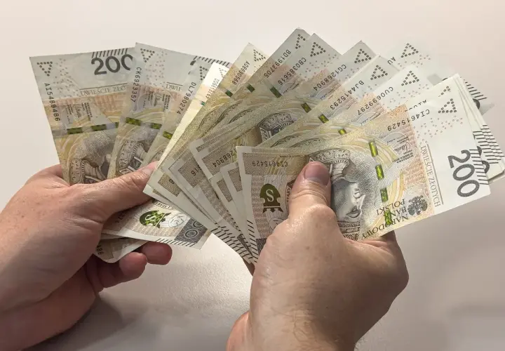 Dwie ręce trzymają wachlarz banknotów po 200 złotych. Czy to duł, czy dół, ważne, że pieniądze są!