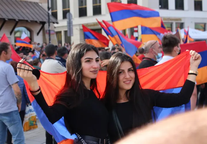 Dwie młode ormianki dumnie prezentują flagę narodową na tle tłumu.
