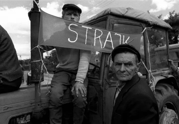 Dwóch mężczyzn w czapkach na tle traktora z banerem "STRAJK".