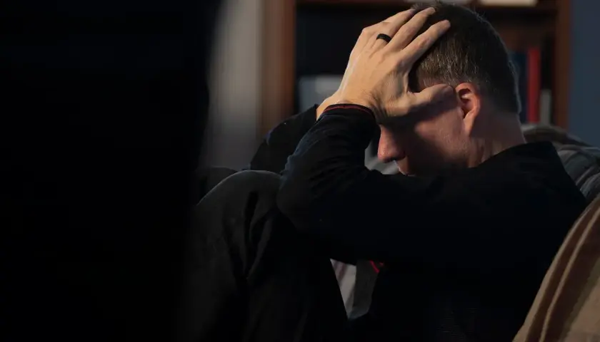 Mężczyzna z rękami na głowie, pogrążony w myślach, być może walczący z glosofobią.