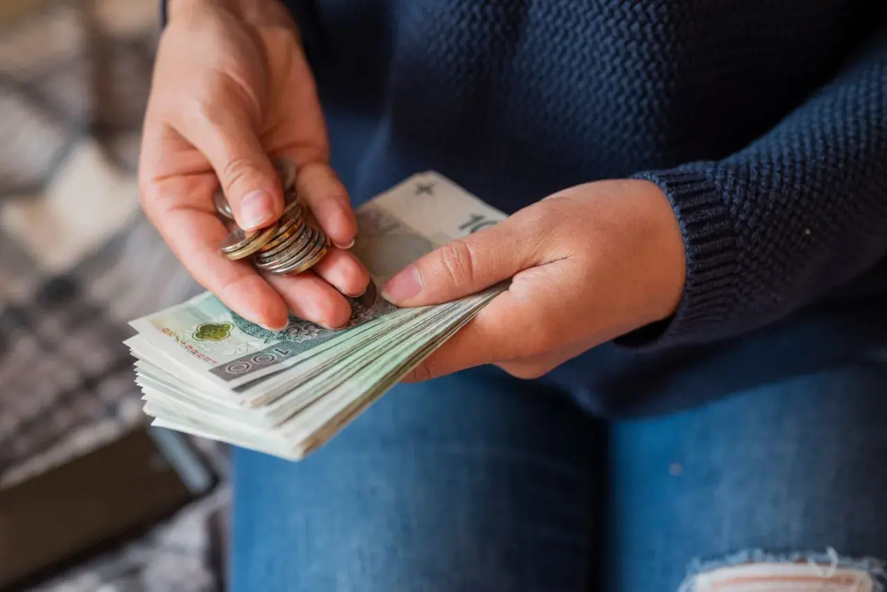 Dłonie liczą banknoty i monety, przygotowując się do wypłaty pensji.