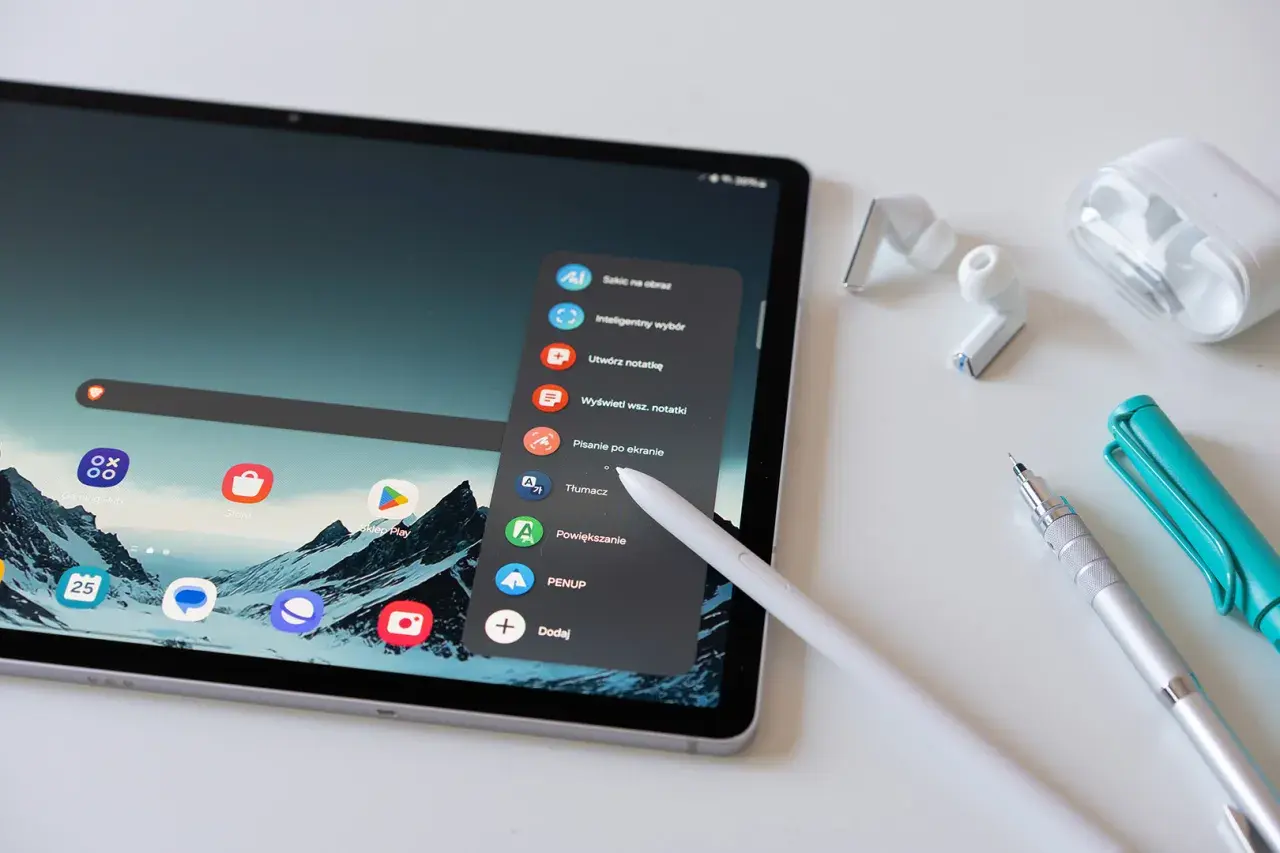 Tablet z rysikiem, słuchawkami i długopisami. Menu tabletu oferuje opcje takie jak "Tłumacz" czy "Sklep Play", co ułatwia kupowanie i kupywanie wirtualnych dóbr.