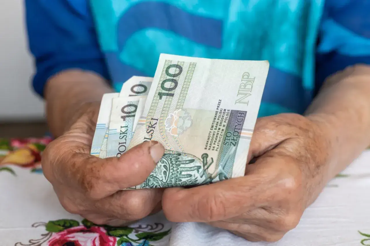 Dłonie trzymają polskie banknoty. Może to symbolizować emeryturę za medal olimpijski, zapewniającą godne życie.