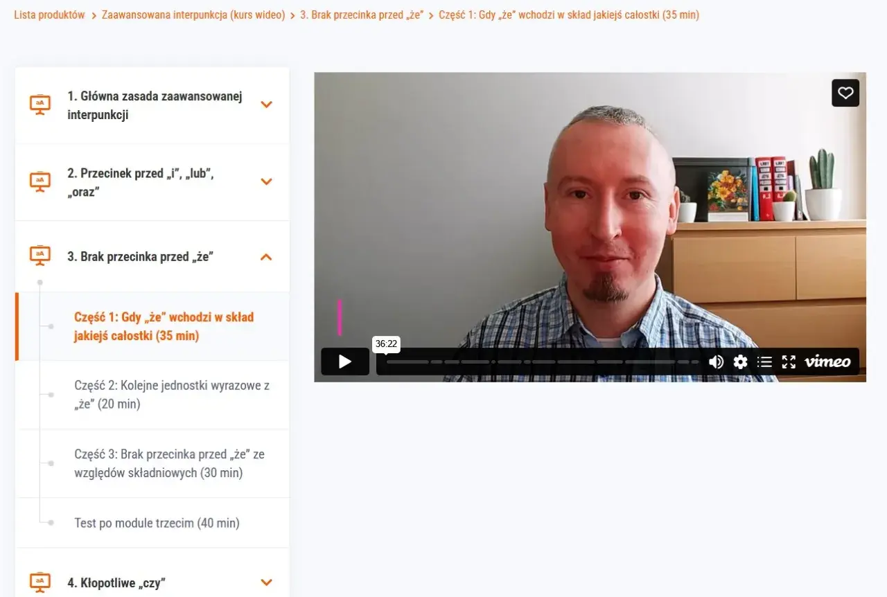 Mężczyzna w kratę tłumaczy, kiedy nie stawiamy przecinka przed "że", omawiając jego użycie w składzie całostki.