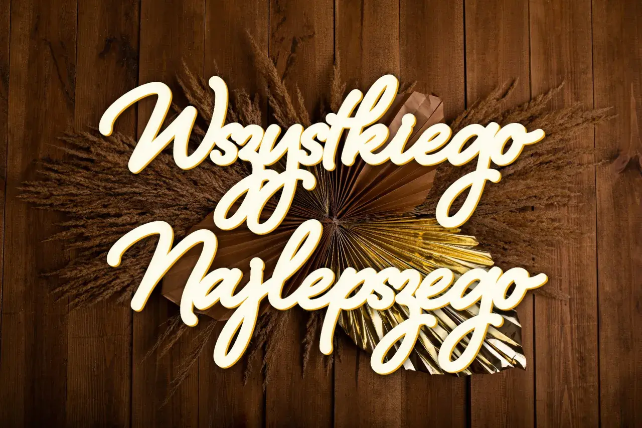 Napis "Wszystkiego najlepszego" ozdobiony suszonymi trawami i złotym wachlarzem na drewnianym tle.
