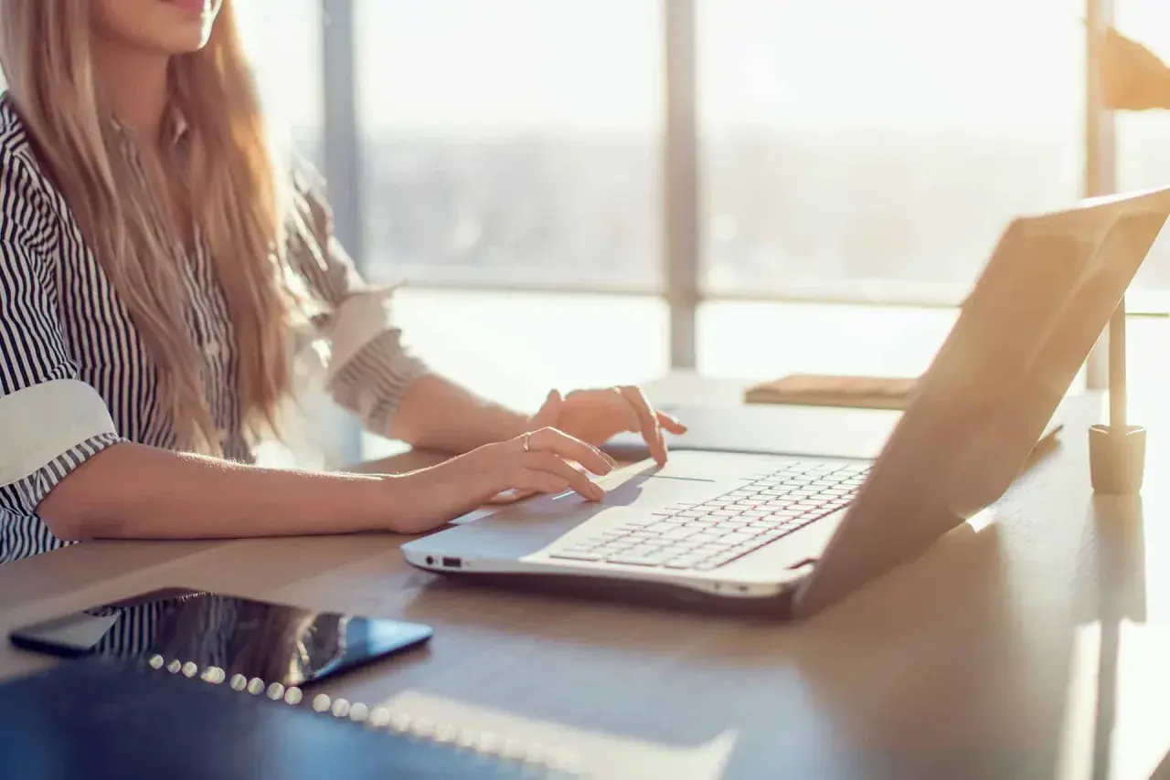 Kobieta z blond włosami pracuje na laptopie w słoneczny dzień.