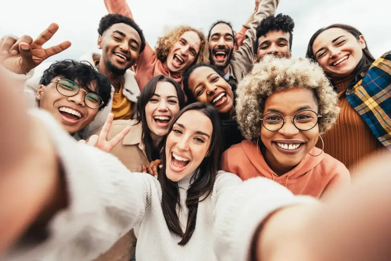 Grupa przyjaciół robi sobie selfie, emanując czystą radością i energią. Uśmiechy od ucha do ucha i gesty pokoju świadczą o ich szczęściu.